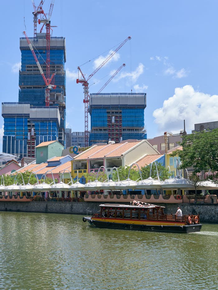A boat navigates a river against a backdrop of colorful buildings and skyscrapers under construction.